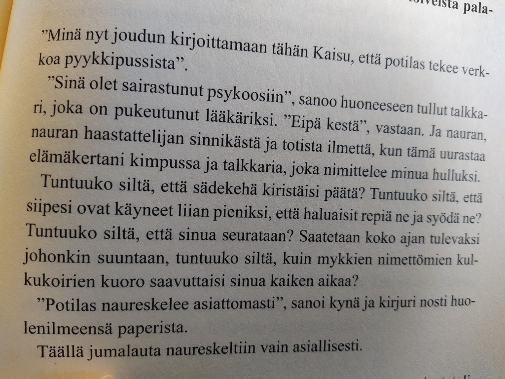 Valokuva kirjan sivusta. Tekstissä lääkäri ja potilas keskustelevat: Sinä olet sairastunut psykoosiin. Potilas tulkitsee henkilön talkkariksi ja ajattelee nauraen muun muassa "Tuntuuko siltä, että siipesi ovat käyneet liian pieniksi, että haluaisit repiä ne ja syödä ne? Lopussa lukee: Potilas naureskelee asiattomasti, sanoi kynä, ja kirjuri nosti huolenilmeensä paperista. Täällä jumalauta naureskeltiin vain asiallisesti.