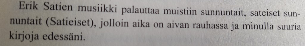 Valokuva kirjan sivusta, jolla lukee: Erik Satien musiikki palauttaa muistiin sunnuntait, sateiset sunnuntait, sulkeissa Satieiset, jolloin aika on aivan rauhassa ja minulla suuria kirjoja edessäni.
