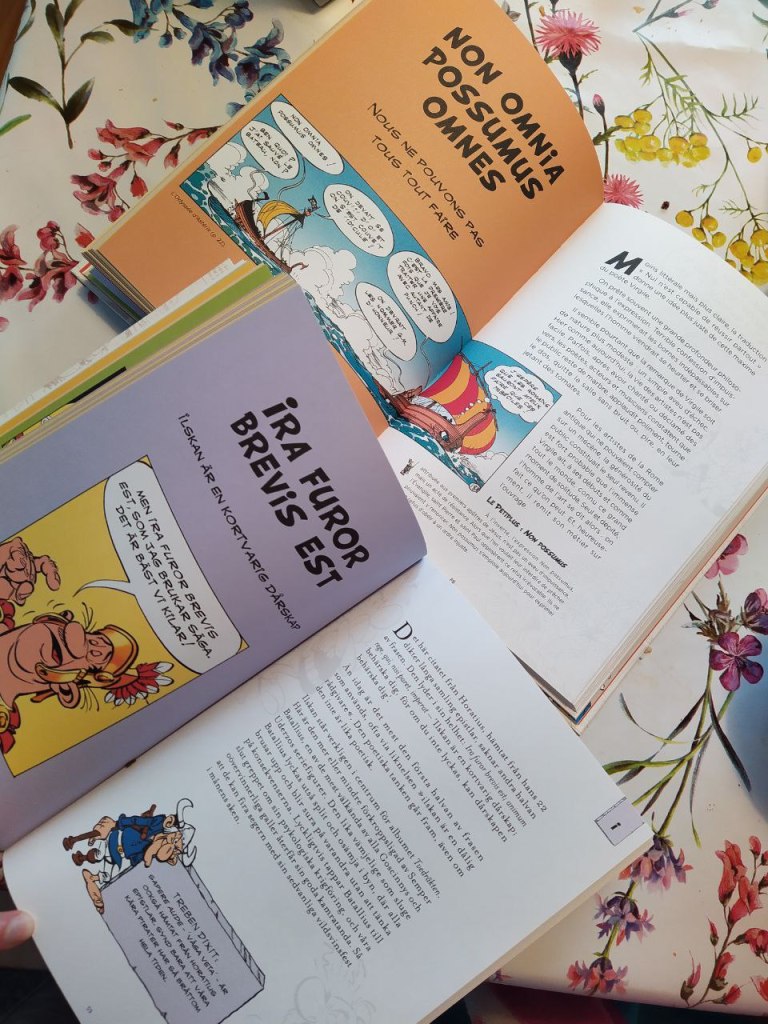 Ranskan- ja ruotsinkielinen kirja levällään pöydällä. Aukeamilla asettelu niin, että vasemmalla ylhäällä latinan fraasi lihavoituna, sen alla käännös ohuella ja niiden alla esimerkkikuva Asterixista. Oikealla sivulla artikkelin tekstimassa ja alimpana pieni lisätietokappale oman alaotsikkonsa alla.