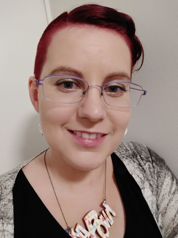 Selfie naamastani, jossa näkyy ripsivärit ja violetit silmälasikehykset. Punainen tukka on toiselta puolelta siili, ja kaulassa on koru, jossa lukee sarjakuvahenkisesti kapow.