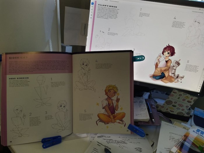 Valokuva, jossa näkyy taustalla kirjan aukeama tietokoneen näytöllä ja sen edessä fyysinen kirja, joka on avattu kirjatukeen sinisten pyykkipoikien avulla. Näytöllä aiheena on Villain's minion ja sen kuvassa vakava mangatyttö rutistaa tyynyä. Kirjassa aiheena on Hero sidekick ja sen kuvassa on pirtsakka mangapoika risti-istunnassa.