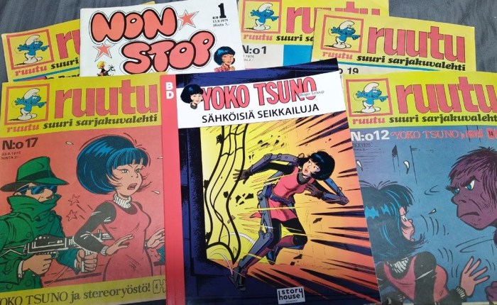 Valokuva sarjakuvien kansista, joista keskimmäisenä on BD-sarjan albumi Sähköisiä seikkailuja ja ympärillä Ruutu-lehtiä ja yksi Non Stop. Sähköisten seikkailujen kannessa on räjähdys, jota Yoko pakenee, ja hänellä on käsissään, jaloissaan ja selkäpuolellaan joitakin mekaanisia, metallisia tukivarsia kehon linjojen myötäisesti. Ruutu-lehdessä vasemmalla oikea gangsterin perikuva painaa aseen piippua Yokon selkää vasten. Oikealla Ruudun kannessa gorillan näköinen hirviö katsoo säikähtänyttä Yokoa.