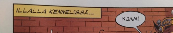 Osa sarjakuvan ruudusta, jossa näkyy vasemman yläkulman kertojanlaatikko. Siinä lukee Illalla kennelissä. Taustalla näkyy tiiliseinää ja oikealla puolella on vilaus koiran korvaa ja legioonalaiskypärää sekä puhekupla Njam.