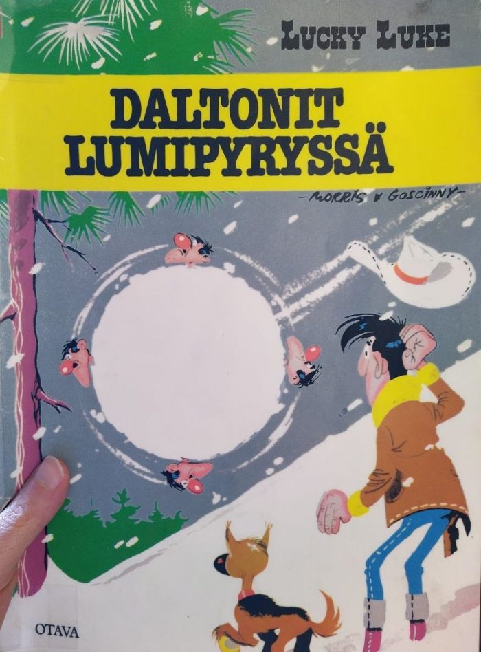Valokuva Daltonit lumipyryssä -albumin kannesta, jossa Lucky Luke ihmettelee takki päällä lumisessa metsämaisemassa Rantanplan-koira vierellään, miten Daltonin veljekset kierivät ohi mäkeä alas yhtenä suurena lumipallona nenät pakkasesta punaisina.